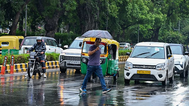 A man holding umbrella walks on a zebra crossing amid rain, in New Delhi. A man holding umbrella walks on a zebra crossing amid rain, in New Delhi.